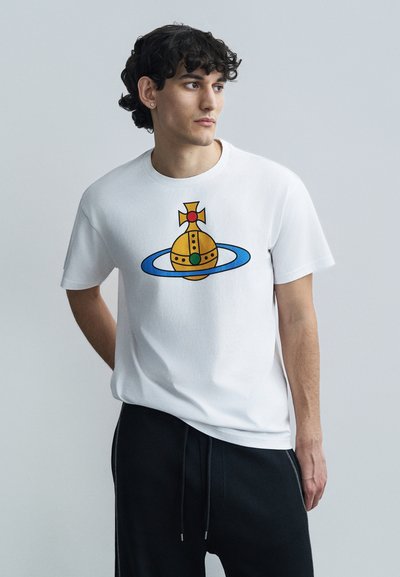 Λευκό βαμβακερό t-shirt με πολύχρωμο γραφικό σχέδιο διαστημόπλοιου με χρυσό σώμα και ανοιχτό μπλε δαχτυλίδι, συνδυασμένο με μαύρο παντελόνι.