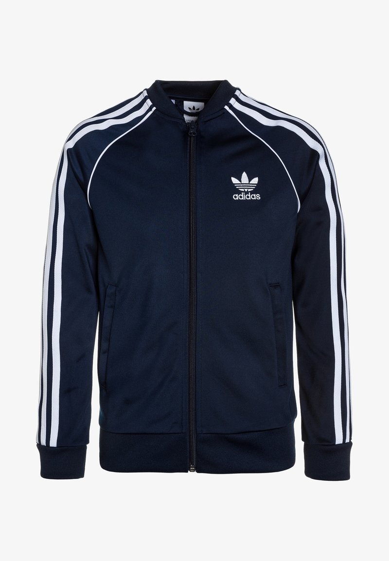 Tummansinisellä Adidas-trainereilla varustettu takki, jossa on valkoinen kolmisauva-muotoilu. Takissa on vetoketjukiinnitys, ribattu hihansuu ja brodeerattu logo rinnassa.