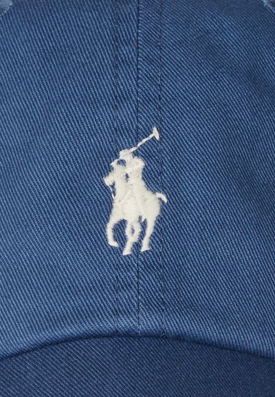 Modra bombažna kapa z belim vezenim logotipom konja in jahača. Tkanina ima teksturiran twill vzorec.
