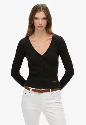 Zwarte geribbelde cardigan met V-hals, lange mouwen en een sluiting met knopen aan de voorkant. Bevat een gouden logo detail en is gestyled met witte jeans en een bruine riem.