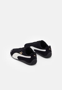 Paire de baskets noires Puma avec bandes latérales blanches et logo Puma doré, vues en angle arrière sur fond blanc.