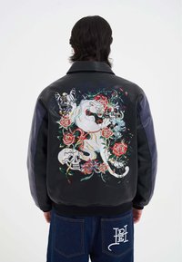 Giubbotto bomber in pelle nera con vivaci ricami di un pantera, fiori, teschi e farfalle sul retro. Accenti blu alle maniche.