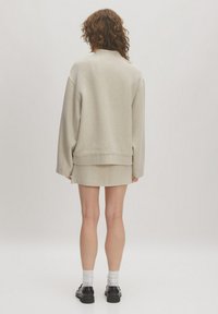 Helles, beiges Oversized-Sweatshirt aus strukturiertem Stoff mit geripptem Saum und überschnittenen Schultern, kombiniert mit einem passenden Minirock.