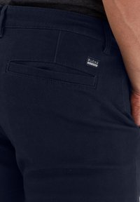Marineblå bukser med en glat stof, der har en baglomme og et lille "BLEND" mærke. Designet er slim fit og moderne.