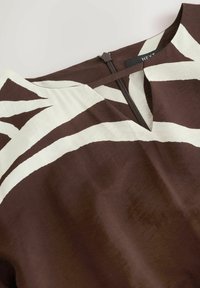 Top marrón con estampado de rayas abstractas blancas, con escote en V y cierre de cremallera en la espalda. Textura de tela suave.