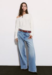 Valkoinen off-shoulder neule, vaaleansiniset leveälahkeiset farkut, ruskea vyö ja mustat korkeat kengät. Sileä pinta ja rento istuvuus.