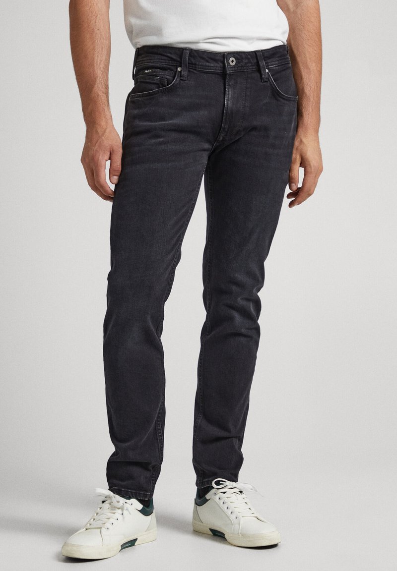 Zwarte denim jeans met een slim fit, vijf zakken, subtiele slijtage. Gekomponieerd met witte sneakers met groene accenten.