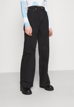 Person wearing high-waist black wide-leg jeans with black platform shoes and a long-sleeve top with blue and white pattern.