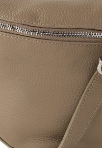 Bruine leren handtas met een gestructureerde afwerking, voorzien van een zilveren rits en contrasterende stiksels. Inclusief een brede, platte band.