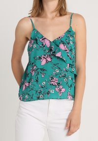 Kamizelka w kwiatowy wzór w odcieniu teal z różowymi i białymi kwiatami. Posiada cienkie regulowane ramiączka oraz falbany wzdłuż dekoltu.