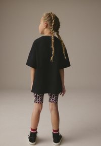 T-shirt oversize noir, leggings à motif floral en rose et noir, baskets montantes noires avec accents rouges, cheveux en deux nattes.
