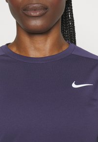 Lila Sportshirt mit Rundhalsausschnitt und kurzen Ärmeln, ausgestattet mit einem weißen Nike-Logo auf der linken Brustseite. Glatte Textur.