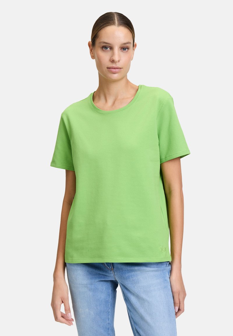 Zielona, teksturowana koszulka z krótkim rękawem i okrągłym dekoltem, z delikatnym wzorem. Połączona z jasnoniebieskimi dżinsami.