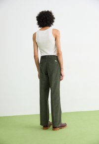 Groene corduroy broek met een hoge taille en een ruime pasvorm, gecombineerd met een witte tanktop. Heeft achterzakken en bruine schoenen met een dikke zool.