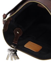 Open brown leather bag with black fabric interior showing attached keyring holding multiple silver keys and a small brown leather patch inside.