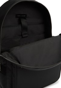 Μαύρο σακίδιο πλάτης Tommy Hilfiger ανοιχτό για να δείχνει το εσωτερικό με επένδυση για λάπτοπ και τσέπη με φερμουάρ.