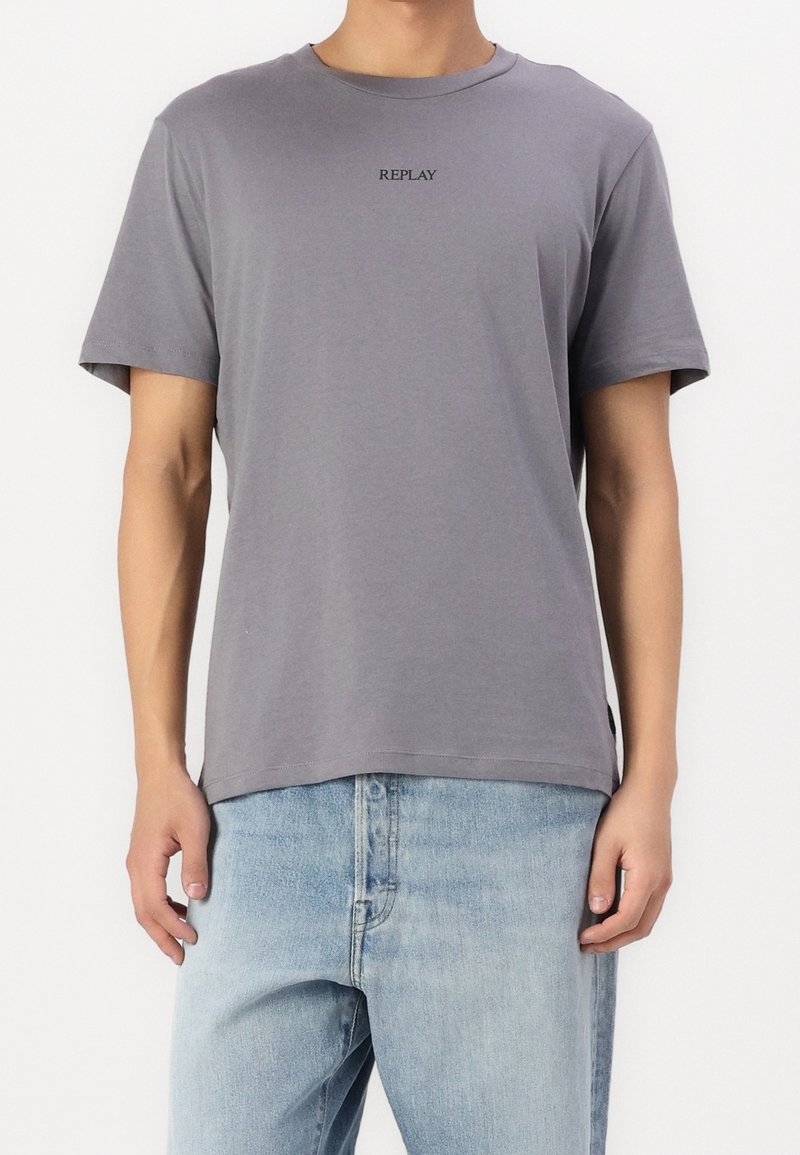Grijze katoenen T-shirt met ronde hals en korte mouwen; heeft een minimalistisch zwart "REPLAY" logo op de borst.