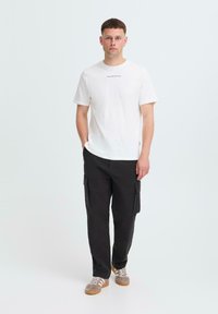 White cotton t-shirt with short sleeves, paired with black cargo pants featuring side pockets, and brown and white sneakers.