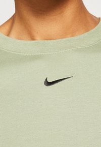 Olivově zelené bavlněné tričko s kulatým výstřihem a krátkými rukávy; na hrudi má černě vyšívané logo Nike.