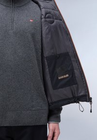 Dunkelgrauer Strickpulli mit hohem Kragen und einem Norwegen-Flaggen-Patch. Innenfutter der schwarzen Pufferjacke mit einer Druckknopftasche und Logo-Detail.