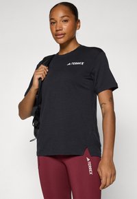 Sort atletisk skjorte med rund halsudskæring, korte ærmer og et diskret TERREX-logo. Båret sammen med bordeaux leggings med sideakcenter.