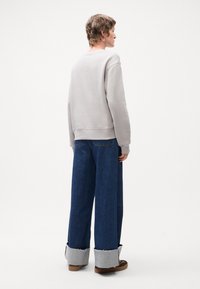 Grå hettegenser med avslappet passform, kombinert med vide jeans i blått med slitte mansjetter. Enkel design med myk tekstur og rene linjer.