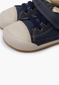 Námořnické modré volnočasové boty s béžovými gumovými špičkami, textilními tkaničkami, suchým zipem a kontrastním prošíváním. Texturovaná gumová podrážka.