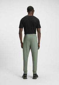 Cropped zwart t-shirt, groene tapered broek met elastische boorden, achterzakdetails, gedragen met donkere schoenen, gladde stoftextuur.
