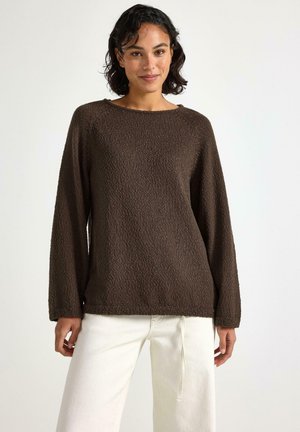 Maglione lungo a maniche, di colore marrone, con un'ampia scollatura, vestibilità rilassata e polsini a coste, abbinato a pantaloni off-white.