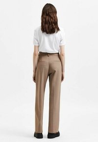 Tan tailored broeken met een rechte pasvorm, gemaakt van een gladde stof. Voorzien van achterzakken en een hoge taille, gecombineerd met een wit T-shirt.