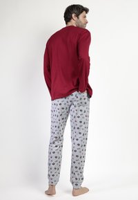 Top de manga larga rojo combinado con pantalones de pijama grises adornados con un patrón de donuts, rayas y diseños divertidos. Tejido de alta calidad y suave.