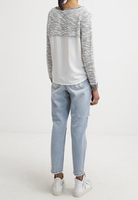 Graues und weißes Strickoberteil mit einem cropped Design, kombiniert mit hellblauen Jeans. Das Outfit bietet eine lässige Passform und weiße Sneaker.