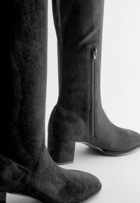 Schwarze Wildleder-Kniehohe Stiefel mit Blockabsatz, seitlichem Reißverschluss und glatter Textur. Das Design ist schlank und enganliegend.