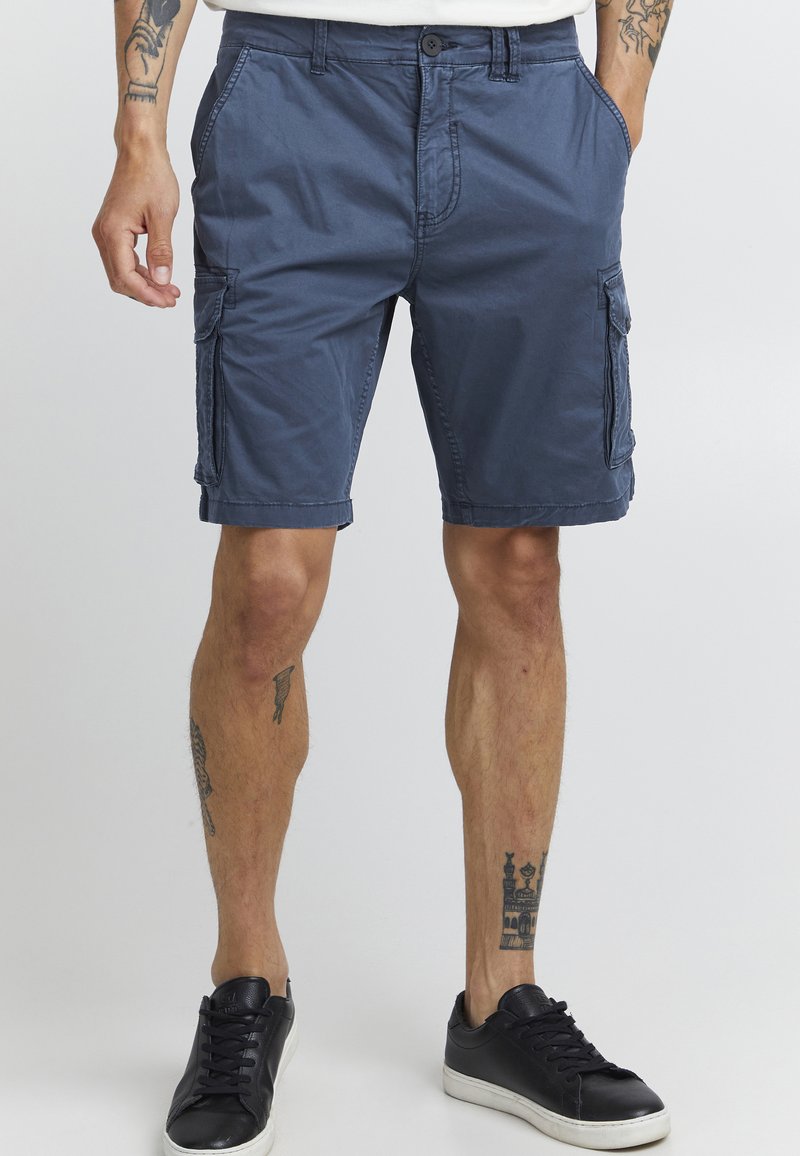 Mørkeblå bomullscargoshorts med sidelommer, beltehemper, knappelukking og med lengde til midt thigh, paret med svarte joggesko.