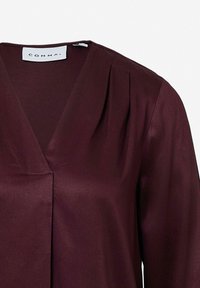 Burgundowa bluzka z dekoltem w kształcie litery V i plisami. Wykonana z gładkiego materiału, z dyskretną metką. Projekt jest prosty, z czystymi liniami.
