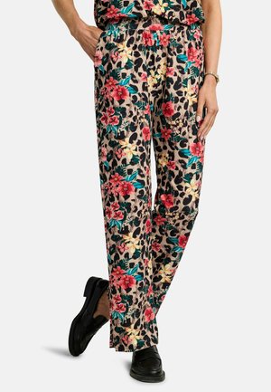 Mujer con pantalones holgados de estampado floral y leopardo combinados con mocasines negros, posando con una mano en el bolsillo y la otra a un lado.