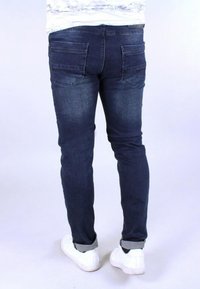 Dark blue denim jeans with a slim fit, featuring back pockets and rolled cuffs over white sneakers. Smooth texture with a classic design.