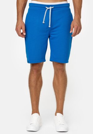 Shorts da uomo blu con coulisse indossati con scarpe da ginnastica bianche, vista frontale dalla vita ai piedi su sfondo bianco.