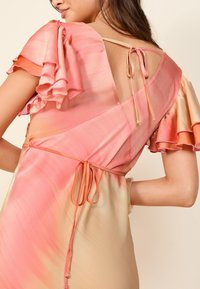 Šaty s prechodom farieb ružovej a broskyňovej, s volánikovými rukávmi, otvoreným chrbtom a šnúrkami. Vyrobené z ľahkej látky, so priliehavým strihom a jemnou textúrou.