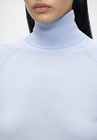 Gros plan d'une personne portant un pull à col roulé bleu clair montrant le cou et le haut de la poitrine.