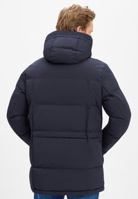 Marineblauer gesteppter Mantel mit Steppmuster, großer Kapuze und langen Ärmeln. Verfügt über einen geraden Saum und eine glatte, matte Oberfläche.