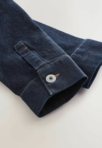 Dark blue denim jeans cuffs with decorative stitching, silver button hardware, and a smooth texture, showcasing a classic design.