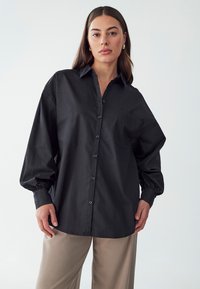 Black button-up shirt with a collar, oversized fit, and long balloon sleeves; features a single chest pocket and smooth texture.