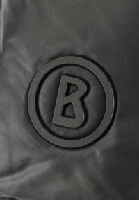 Zwarte textielstof met een ronde reliëf-logo met de opvallende letter 'B' in het midden. Gladde afwerking met matte details.