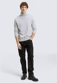 Pulover cu guler înalt de culoare gri deschis, dintr-un tricot moale, asortat cu blugi negri și cizme negre. Croiala este obișnuită, cu tiv și mansete cu dungi.