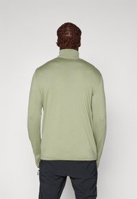 Lys grøn, langermet genser med høy hals i ribbestrikket tekstur og avslappet passform, med rett kant.