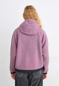 Chaqueta de forro polar púrpura con capucha, que presenta un diseño bordado tonal y el logo "WIP" en la parte posterior. Detalles con puños y dobladillo acanalados.