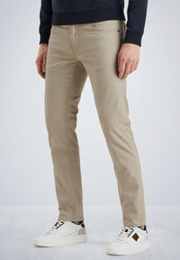 Jeans kaki au design ajusté et en tissu texturé. Comprend des poches, des coutures discrètes, associés à des baskets blanches.