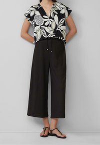 Svart- och vitmönstrad blus med korta ärmar och v-ringning, kombinerad med lösa, mörka byxor och svarta platta sandaler.