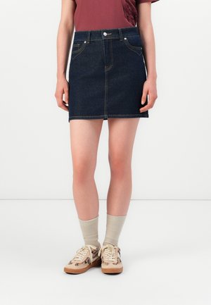 Personne portant une mini-jupe en jean bleu foncé, un haut bordeaux, des chaussettes beige et des baskets beige avec des accents imprimés léopard.